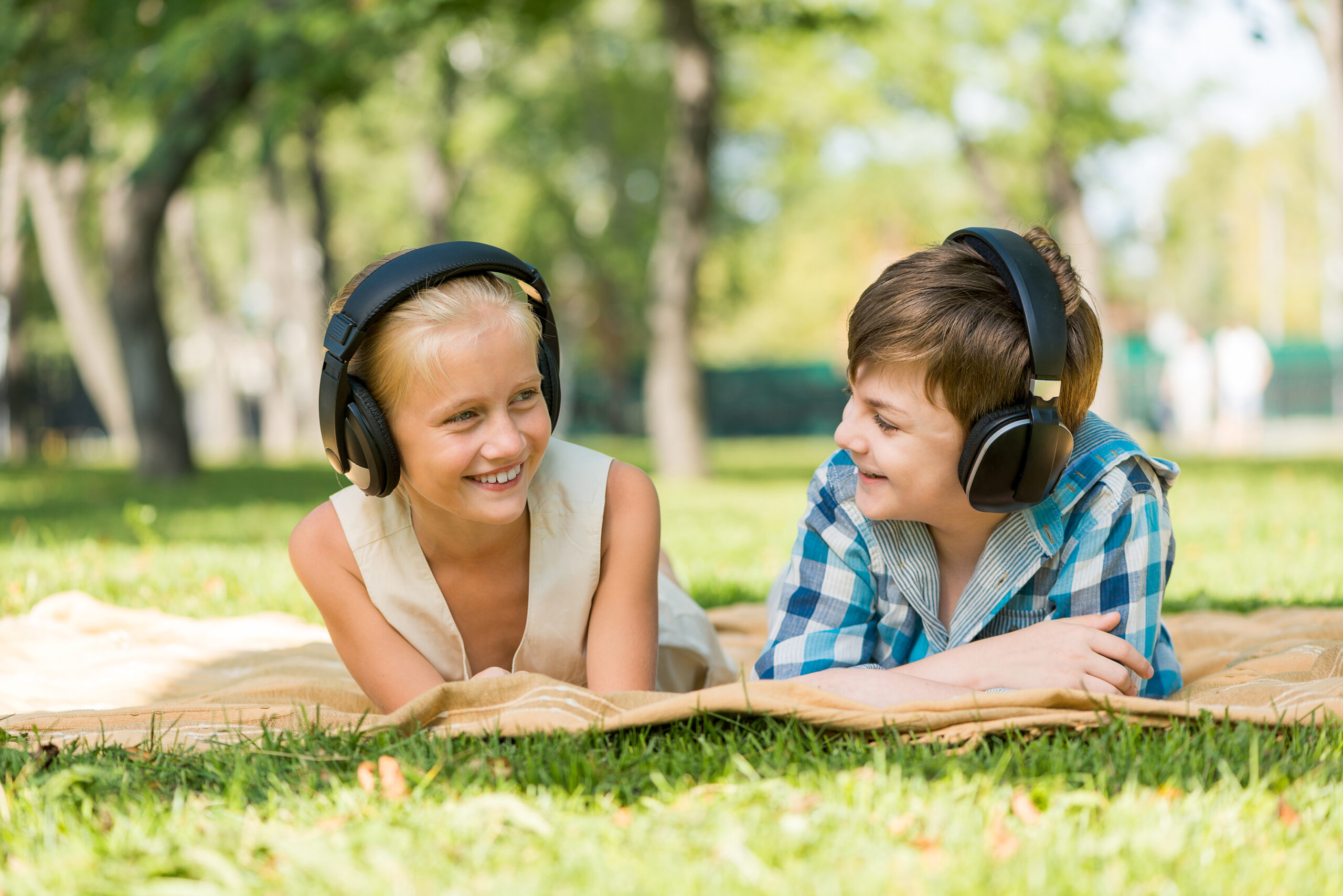 Cute girl and boy lying in park and listen to music
